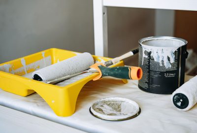 roller and brush in a tray. Metal jar with grey paint on the table. Renovation home concept. Image with selective focus